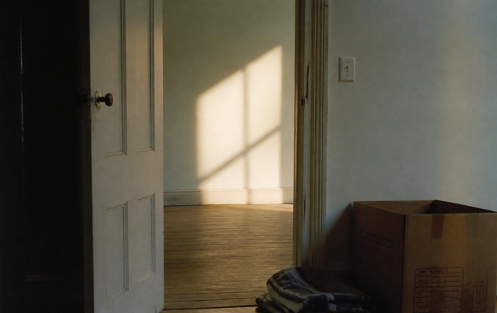 Una puerta abierta en una habitación casi vacía, con una caja y una manta doblada