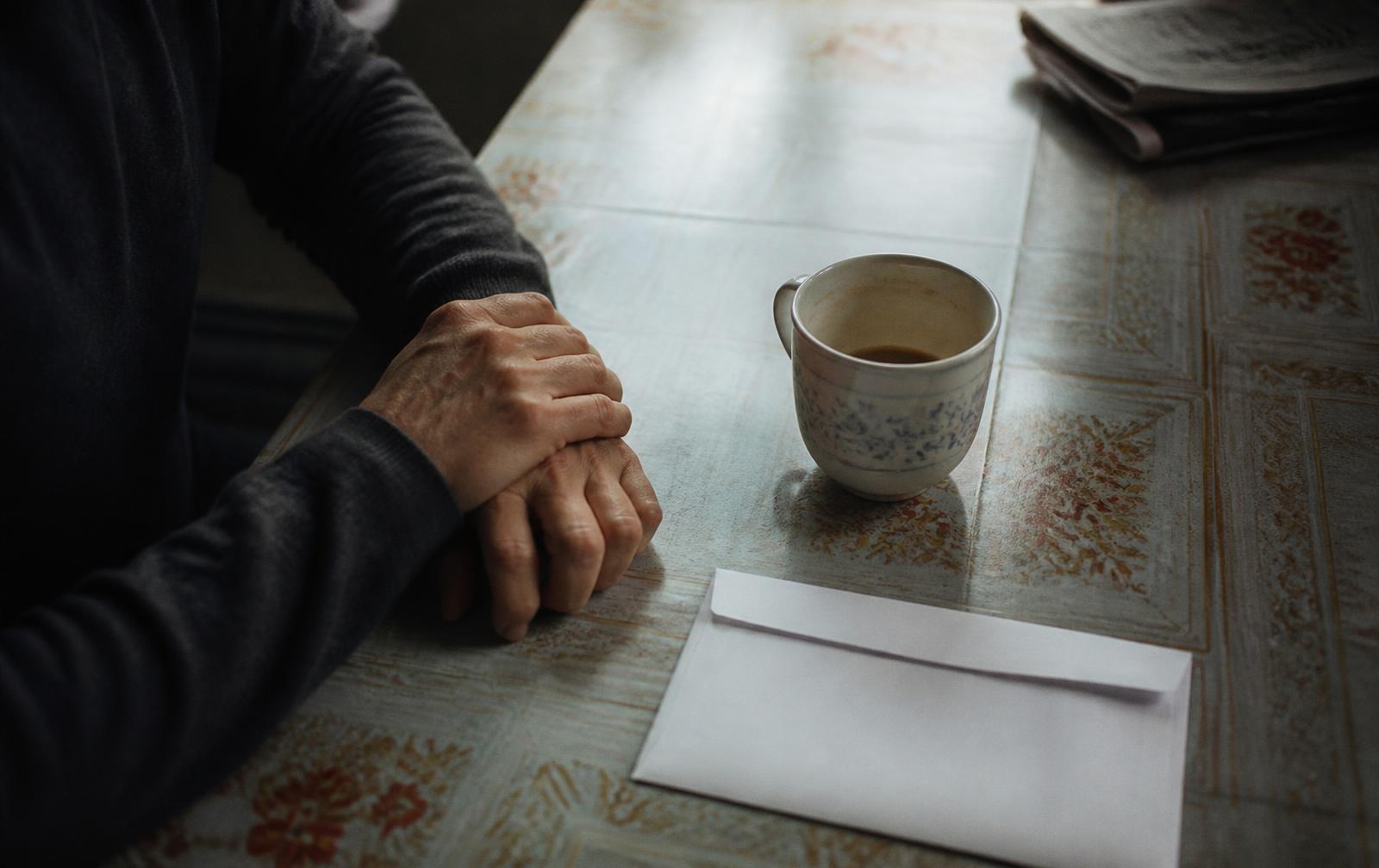 Manos quietas sobre una mesa, junto a una taza y un sobre sin abrir